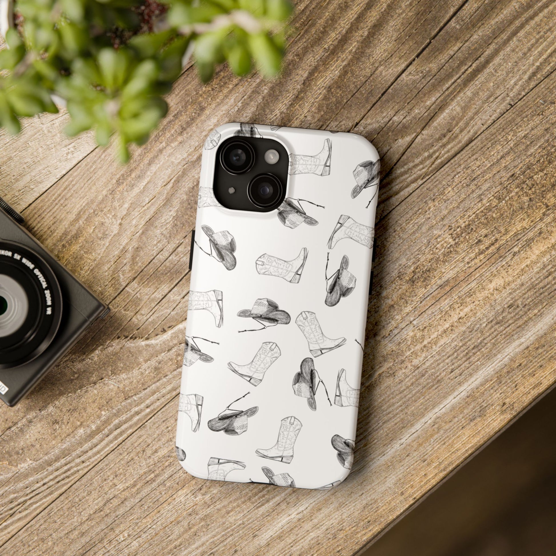 Lifestyle view of Cowgirl Hat & Boot Pattern Phone Case on rustic desk Featuring a charming Western design, this case is perfect for country lovers, rodeo fans, and anyone who adores the country.