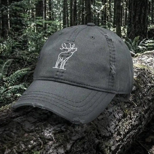 Dark gray cap with a white bugling elk embroidery on a log in a forest setting