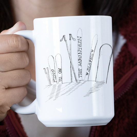 Model holding this 15oz ceramic mug is perfect for anyone who loves the thrill of the slopes and cozy mornings. Featuring a minimalist pen-and-ink illustration of skis and a snowboard stuck in snow, accompanied by the hand-written phrase Find Us on the Mountain Slopes, this mug captures the essence of winter adventures.