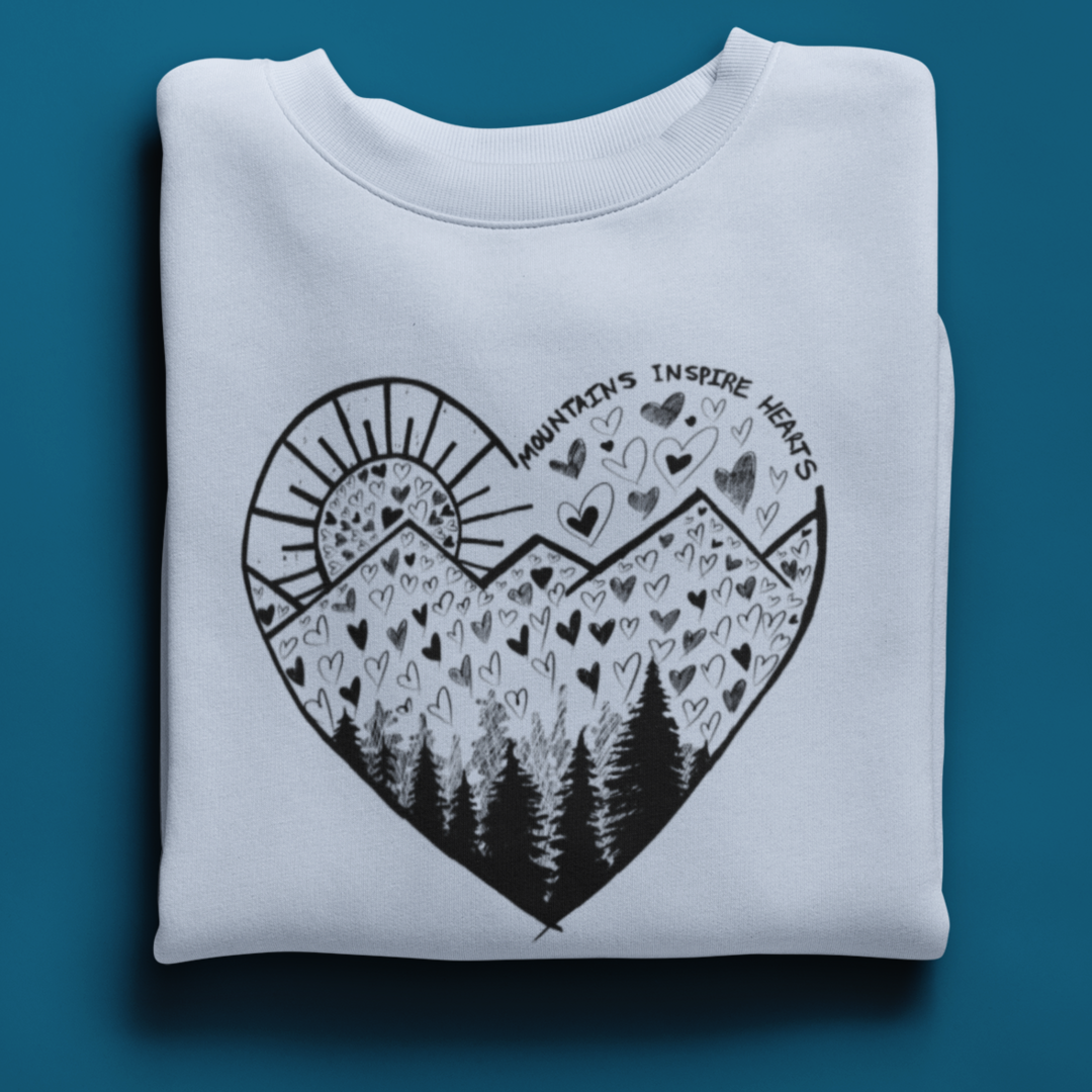 A folded crewneck sweatshirt on blue background featuring a heart-shaped mountain design with the text and Mountains Inspire Hearts, perfect for anyone that loves hiking, mountain views, or the outdoors.