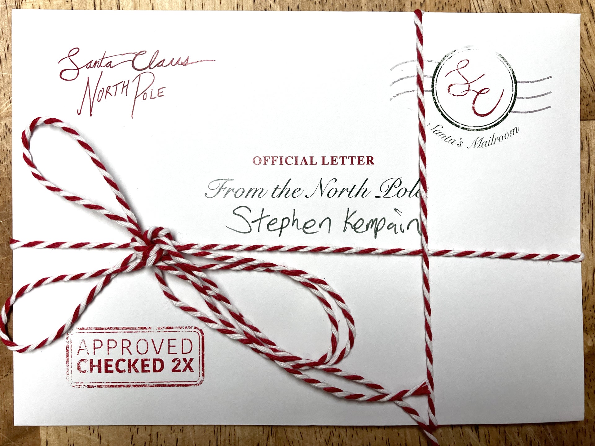 Personalized letter from Santa, fully assembled with a candy cane bow and wax seal, placed on a table. The envelope shows intricate details, adding a festive and custom touch to the holiday letter.