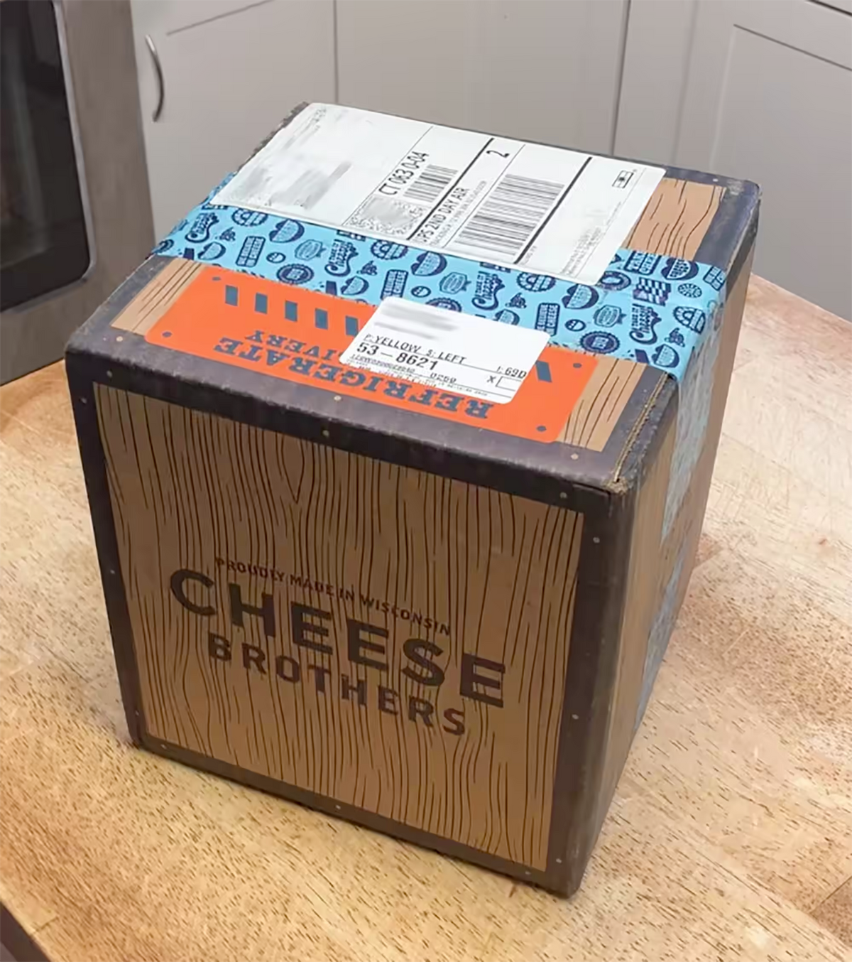 A Cheese Brothers shipping box on wooden butcher block showing how the Cheese Brothers ship their cheeses. The box is insulated and equipped with cold packs to temperature control the cheese.