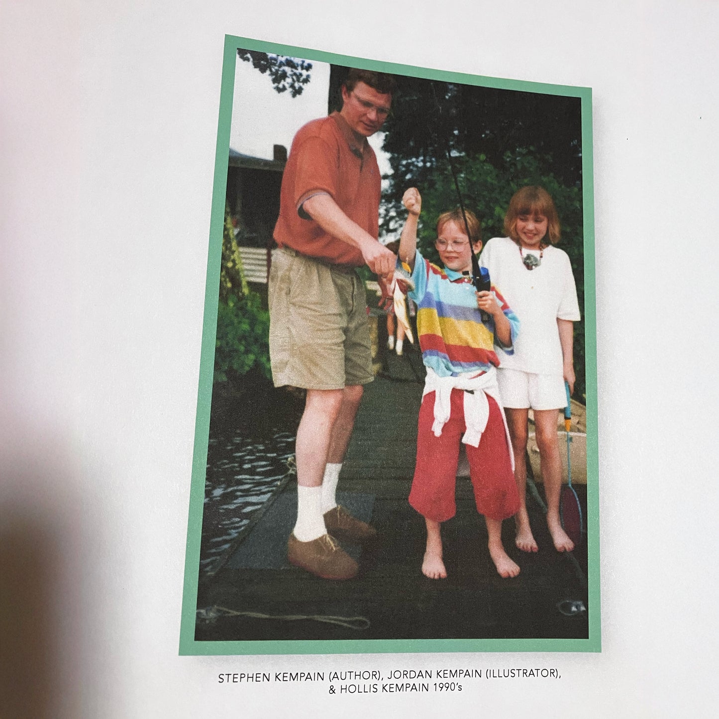 A picture of the Kempain family in the 1990s. Stephen Kempain (Author), Jordan Kempain (Illustrator), and Hollis Kempain on a fishing dock holding a bass.