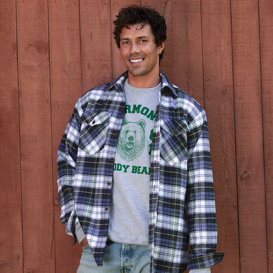 Man wearing a plaid shirt over a graphic t-shirt against a wooden wall