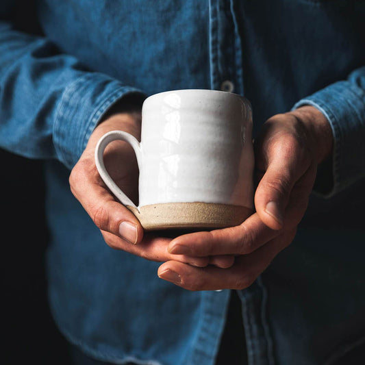 Person holding a white ceramic mug with a dark background