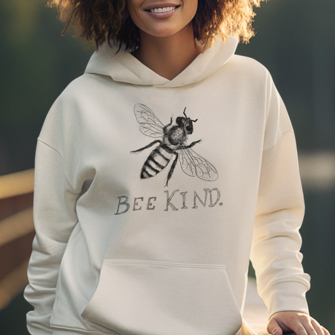 Woman wearing sand-colored Bee Kind hoodie with an illustrated bee design, cute graphic sweatshirt for nature lovers and kindness gifts.