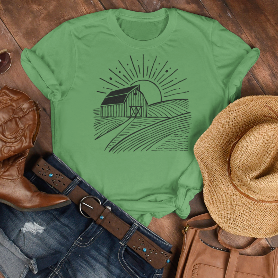Green Farm Barn Scene T-Shirt laid out on a rustic wood floor with jeans, a cowgirl hat, and boots, creating a stylish country-inspired outfit for farmers and country living enthusiasts.