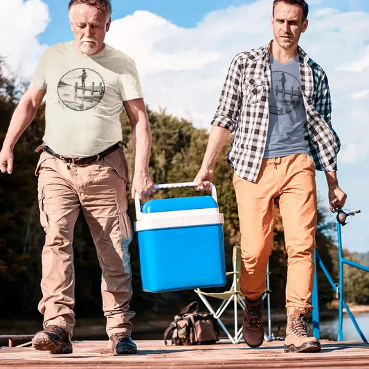 Models wearing Fisherman Dockside Tee, featuring a geometric illustration of a fisherman on a dock, perfect for anglers and outdoor enthusiasts. The models are carrying cooler and fishing pole getting ready for a day of fishing while sporting their matching fishing tees. One is wearing blue color and one is wearing sand color option.