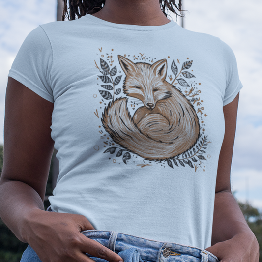 Women's Fox in the Ferns T-Shirt worn by a model, featuring a cozy illustrated fox curled up among lush ferns in a nature-inspired design.