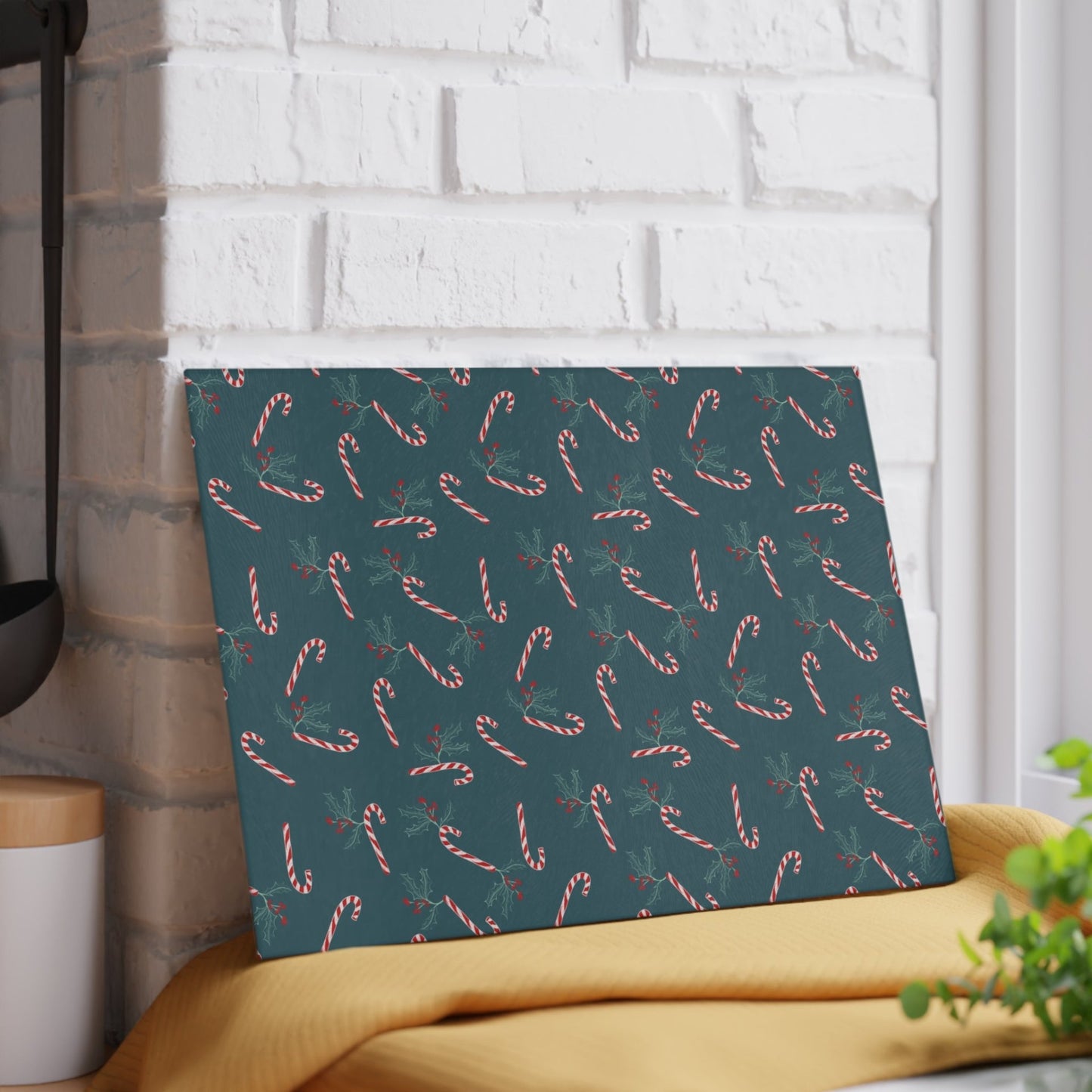 Glass cutting board with a candy cane and holly pattern, leaned horizontally against a wall in a kitchen setting, showcasing its festive holiday design.