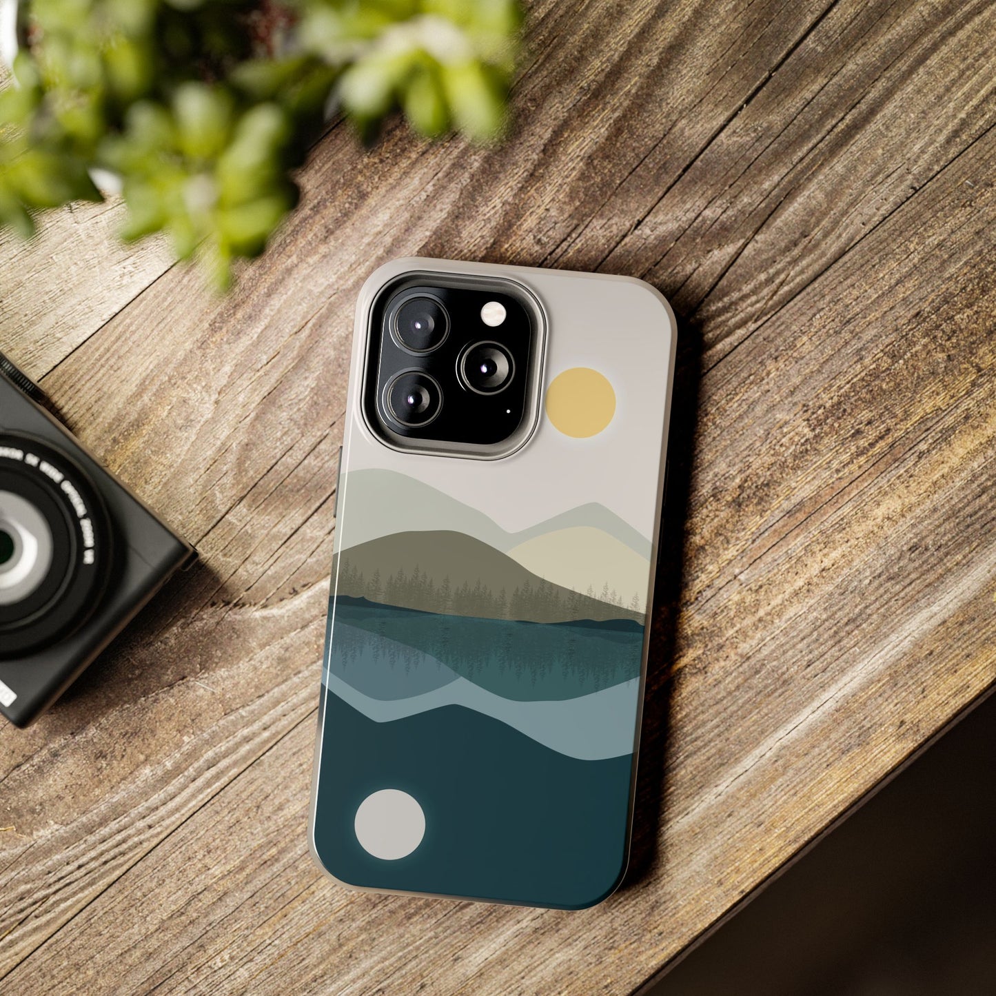 Phone case with an abstract illustration of a mountain reflected on a lake, placed on a desk, designed for iPhone and Samsung models, showcasing its nature-inspired style in a casual setting.