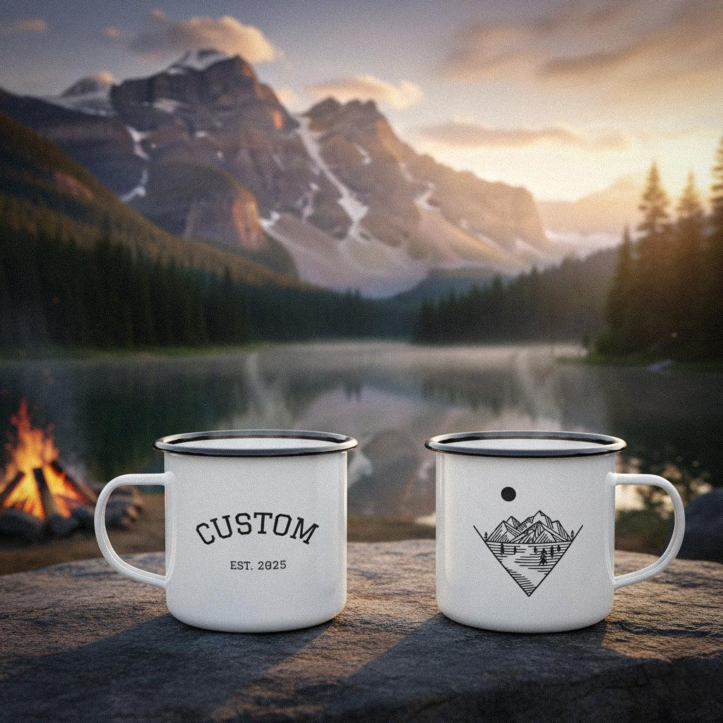 Two personalized camping mugs on a rock by a mountain lake with a campfire.