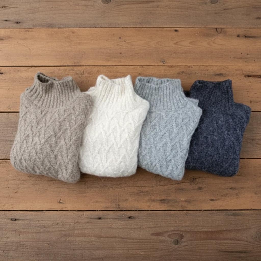 Four alpaca knitted vests in different colors on a wooden surface