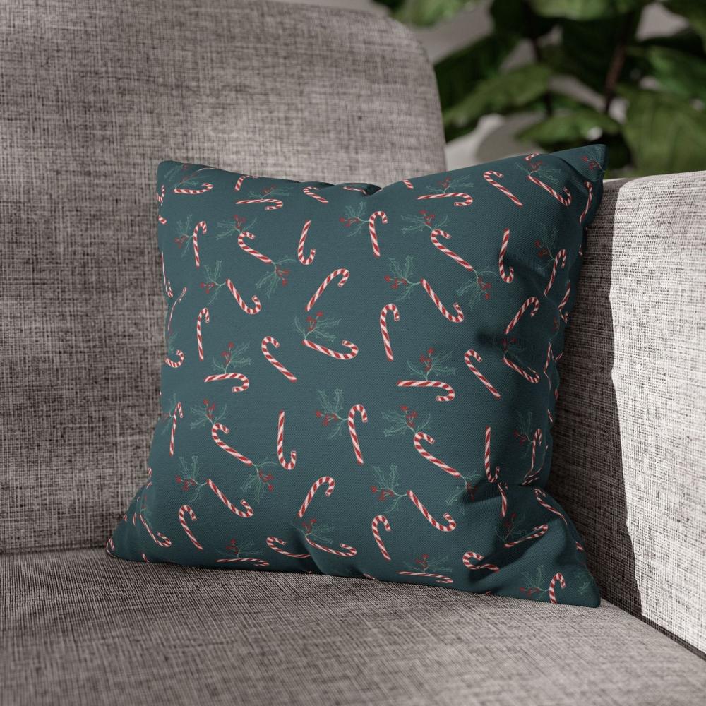 Lifestyle view of a square pillow case featuring a candy cane and holly pattern, placed on a couch in a cozy living room setting, perfect for holiday decor.
