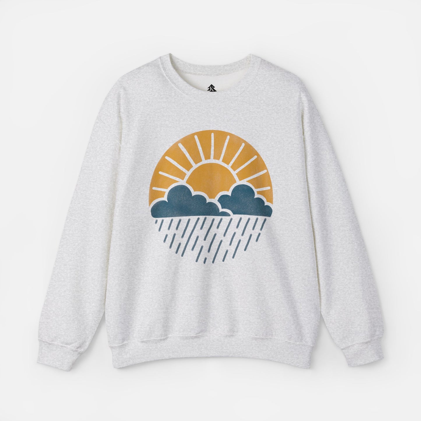 Flat lay of Sun Over Clouds Minimalist Sweatshirt in grey fabric on a white background, featuring a simple line art illustration of a sunrise over clouds and rain within a subtle circle, printed on a classic unisex crewneck.