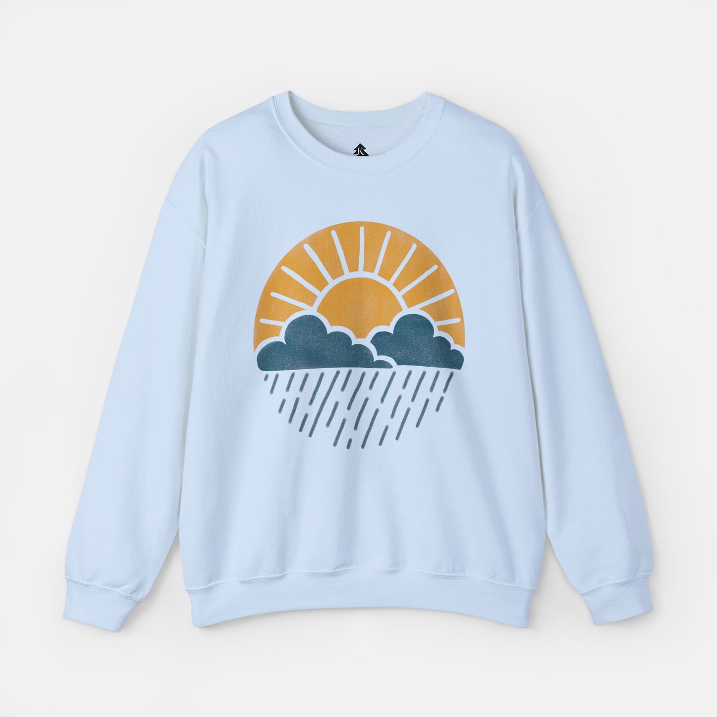 Flat lay of Sun Over Clouds Minimalist Sweatshirt in light blue fabric on a white background, featuring a simple line art illustration of a sunrise over clouds and rain within a subtle circle, printed on a classic unisex crewneck.