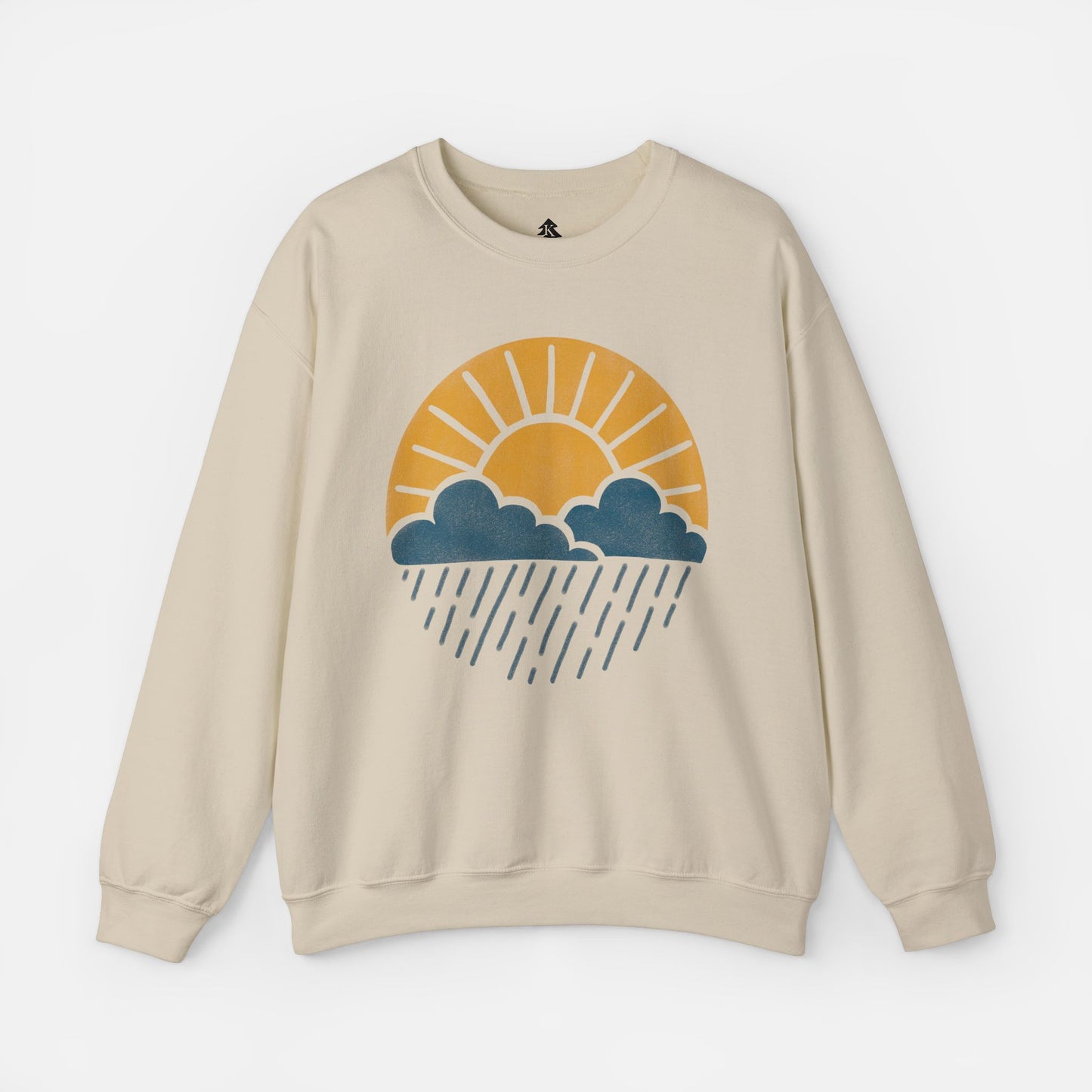 Flat lay of Sun Over Clouds Minimalist Sweatshirt in sand color fabric on a white background, featuring a simple line art illustration of a sunrise over clouds and rain within a subtle circle, printed on a classic unisex crewneck.