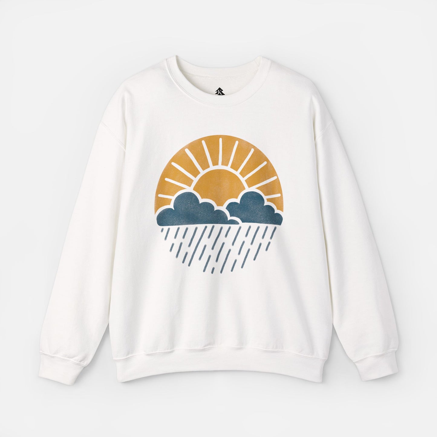 Flat lay of Sun Over Clouds Minimalist Sweatshirt in white fabric on a white background, featuring a simple line art illustration of a sunrise over clouds and rain within a subtle circle, printed on a classic unisex crewneck.