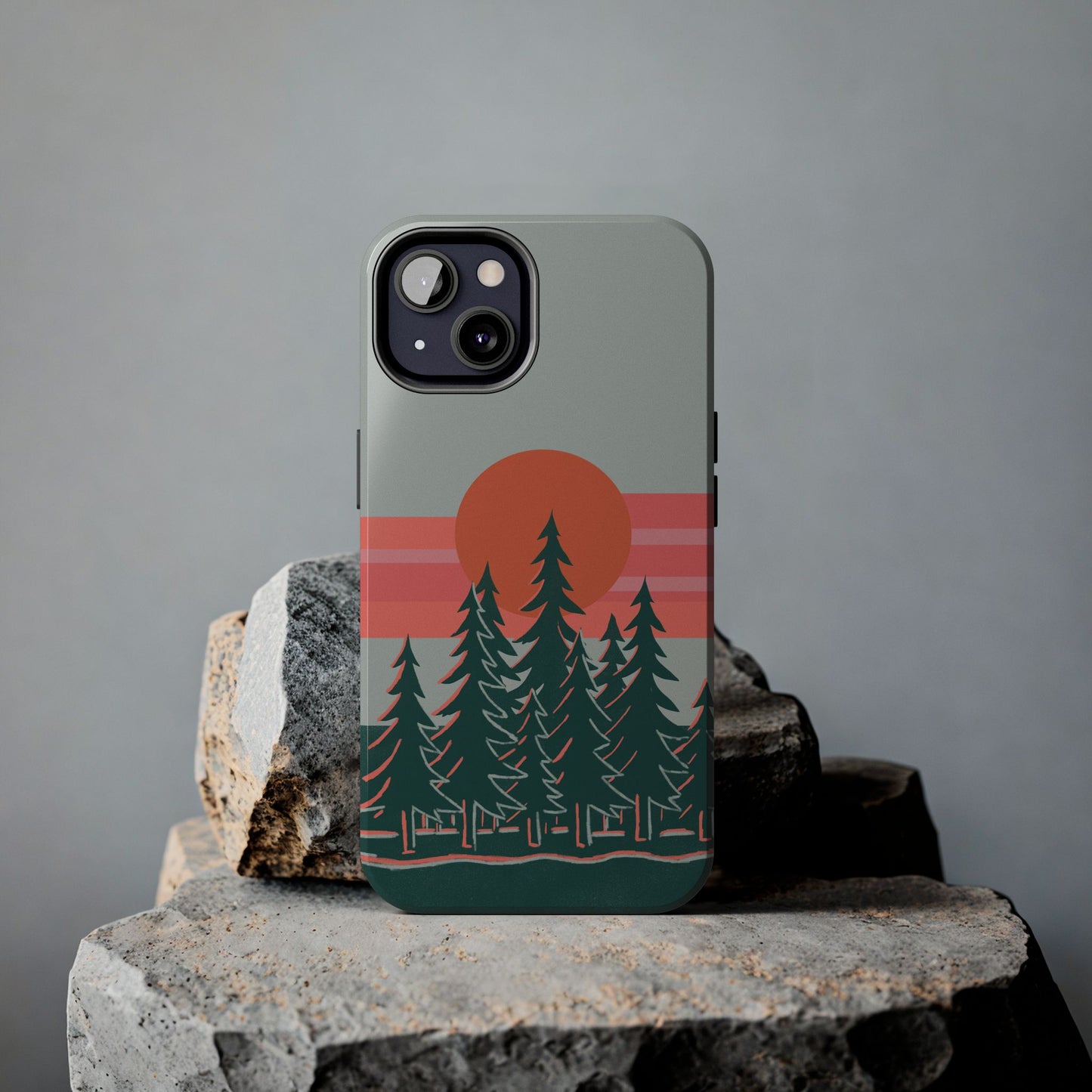 Sunset Pines Phone Case displayed on a rock, featuring a sunset sky and pine trees illustration.