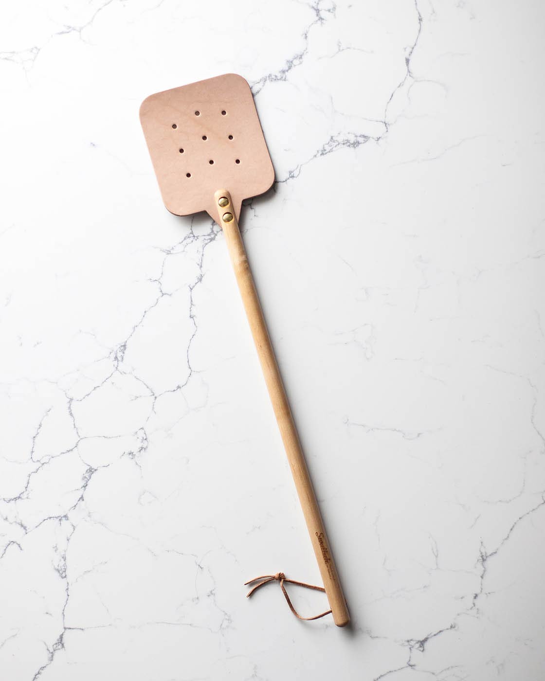 The maple color Leather Huntsman Flyswatter by Farmhouse Pottery on a white marble background sold by Kempain Family Outfitters.