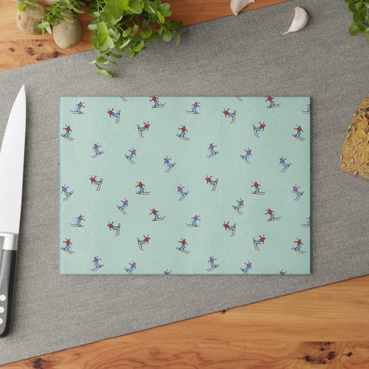 Top view of a glass cutting board featuring an illustrated skier pattern, titled 'Carving the Slopes,' placed on a kitchen table, adding a winter sports-inspired touch to the kitchen decor.