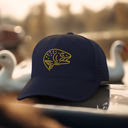Front view of Trout Head Trucker Cap on boat edge with lake background, featuring bold embroidered trout head silhouette on structured navy front panel with matching mesh sides and back.
