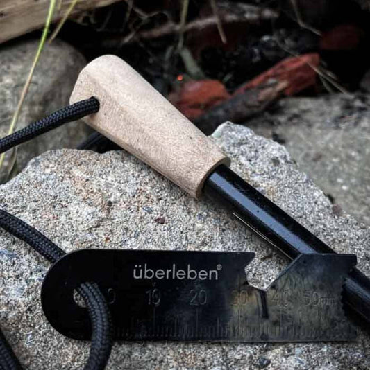A traditional hand crafted ferro rod fire starter on a rock near a campfire.