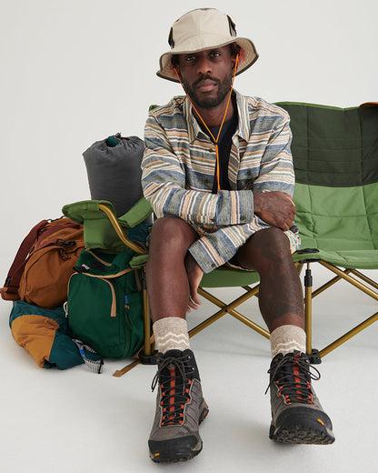 A man wearing a Khaki color 100% Organic Cotton Utility Bucket Hat by United By Blue sitting near camp gear.