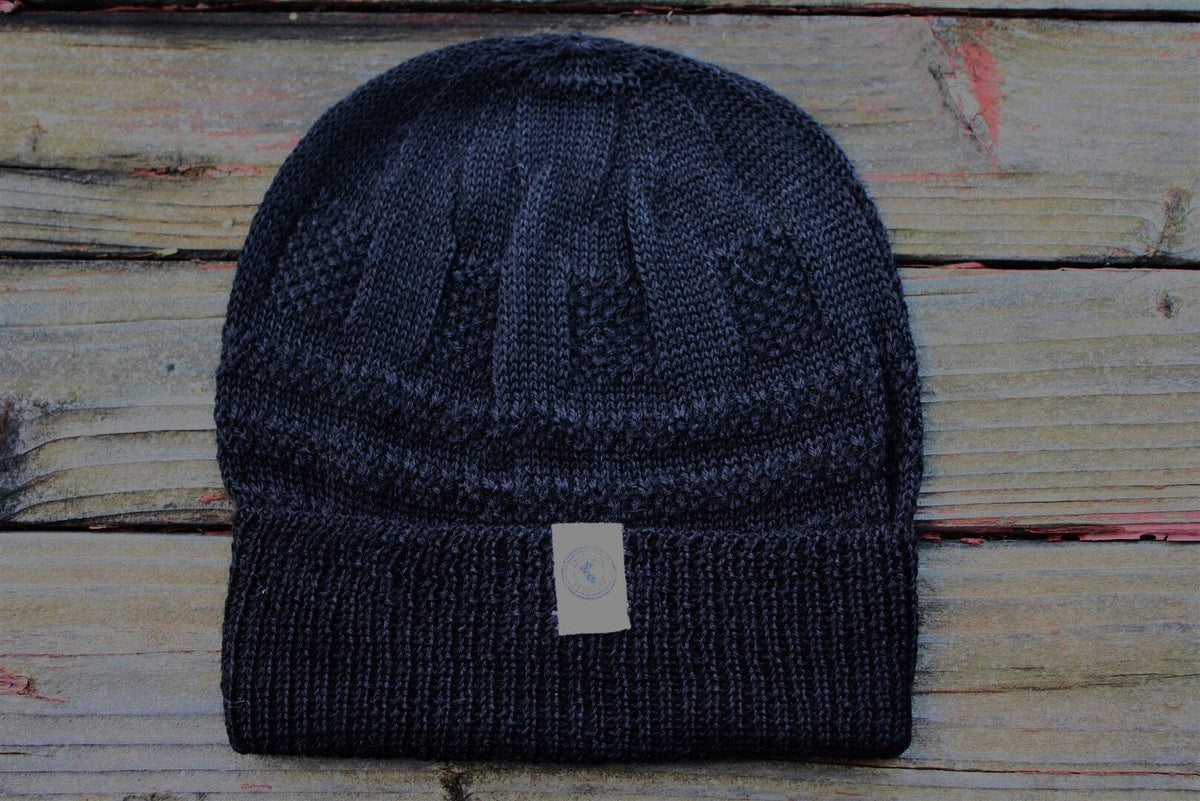 A navy color 100 percent baby alpaca knit winter hat by Purely Alpaca displayed on a wooden surface.