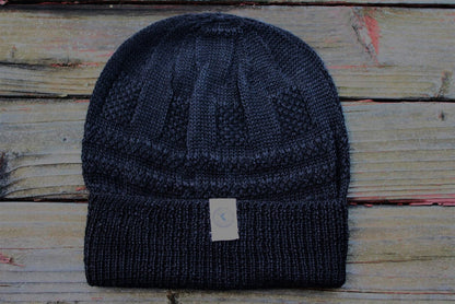 A navy color 100 percent baby alpaca knit winter hat by Purely Alpaca displayed on a wooden surface.