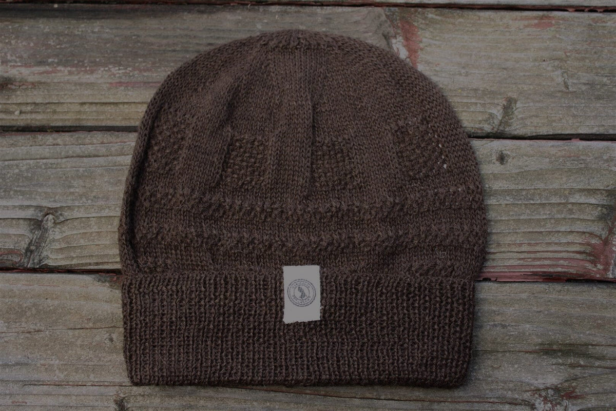 A brown 100 percent baby alpaca knit winter hat by Purely Alpaca displayed on a wooden surface.