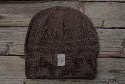 A brown 100 percent baby alpaca knit winter hat by Purely Alpaca displayed on a wooden surface.