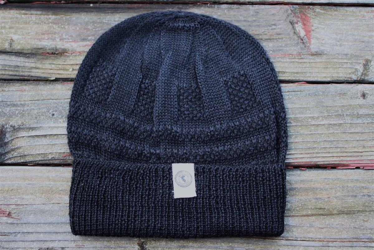 A blue 100 percent baby alpaca knit winter hat by Purely Alpaca displayed on a wooden surface.