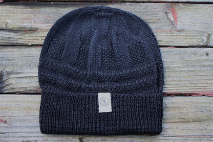 A blue 100 percent baby alpaca knit winter hat by Purely Alpaca displayed on a wooden surface.