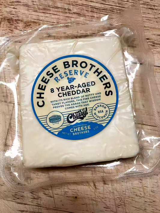 A vacuum-sealed package of Cheese Brothers Reserve 8 Year-Aged Cheddar Cheese on a light wood surface, with a large blue and white circular label on the front.