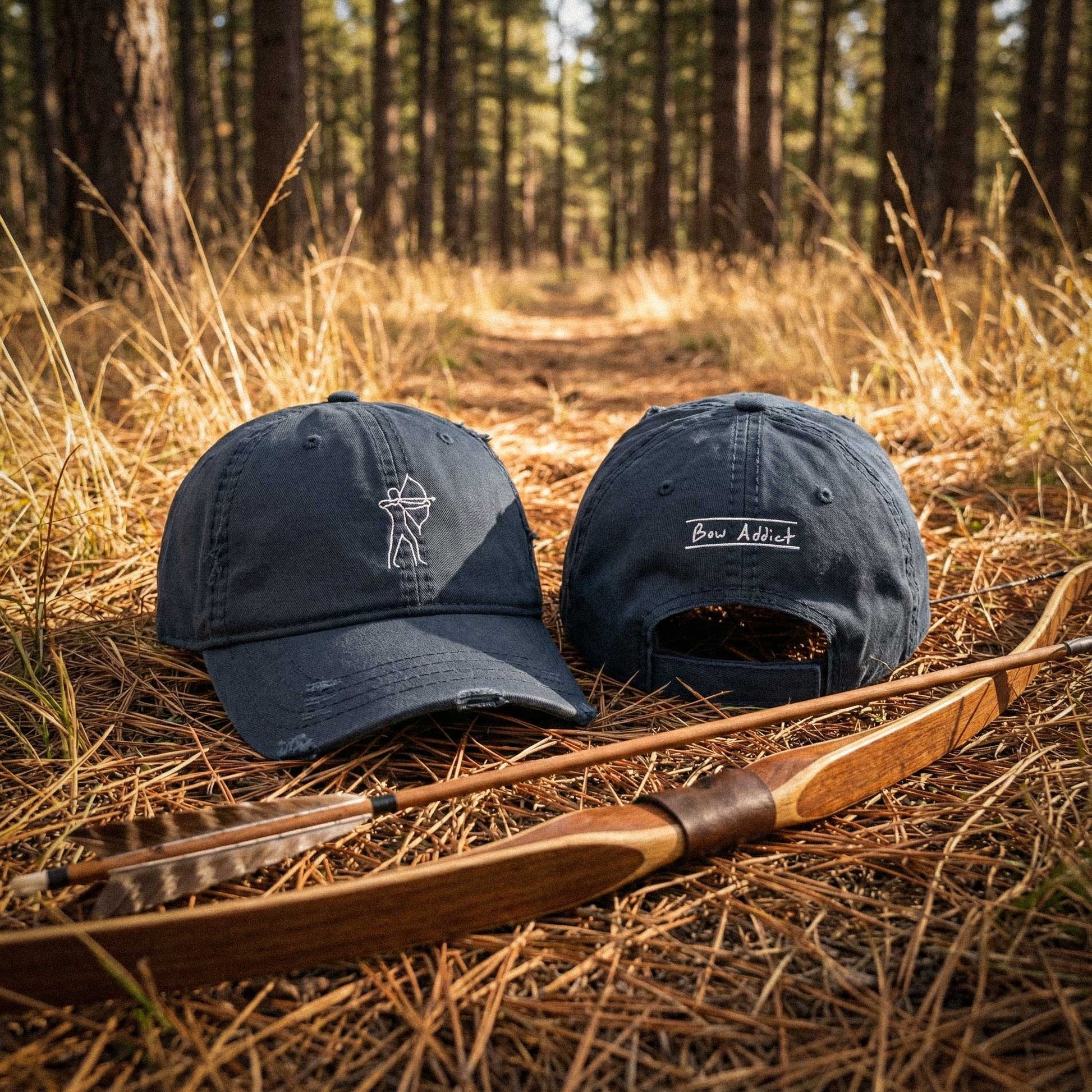 Two navy blue caps with archery symbols on a wooden bow and arrow in a forest setting.