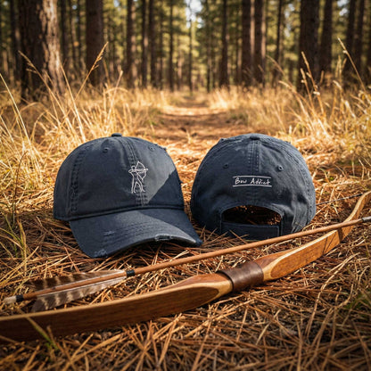Two navy blue caps with archery symbols on a wooden bow and arrow in a forest setting.