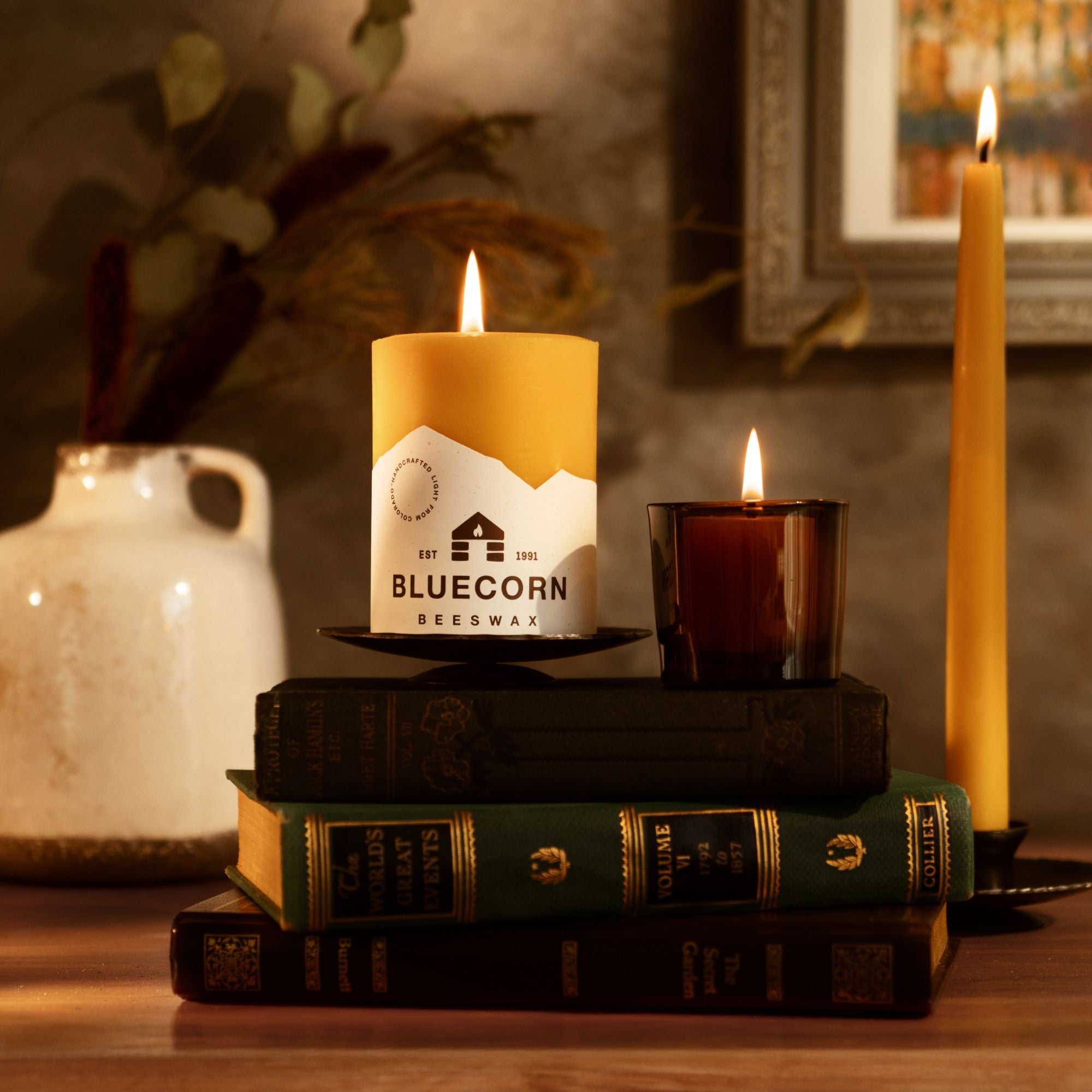 Candle with 'Bluecorn' branding on a stack of books with a warm glow.