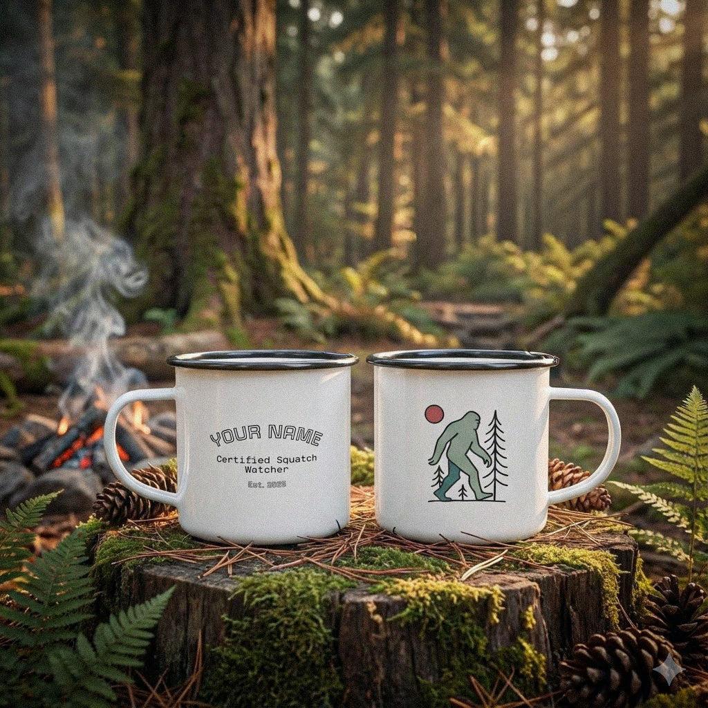 Two enamel mugs on a log in a forest setting with a campfire featuring customizable text on one side with Bigfoot graphic by Kempain Family Outfitters.