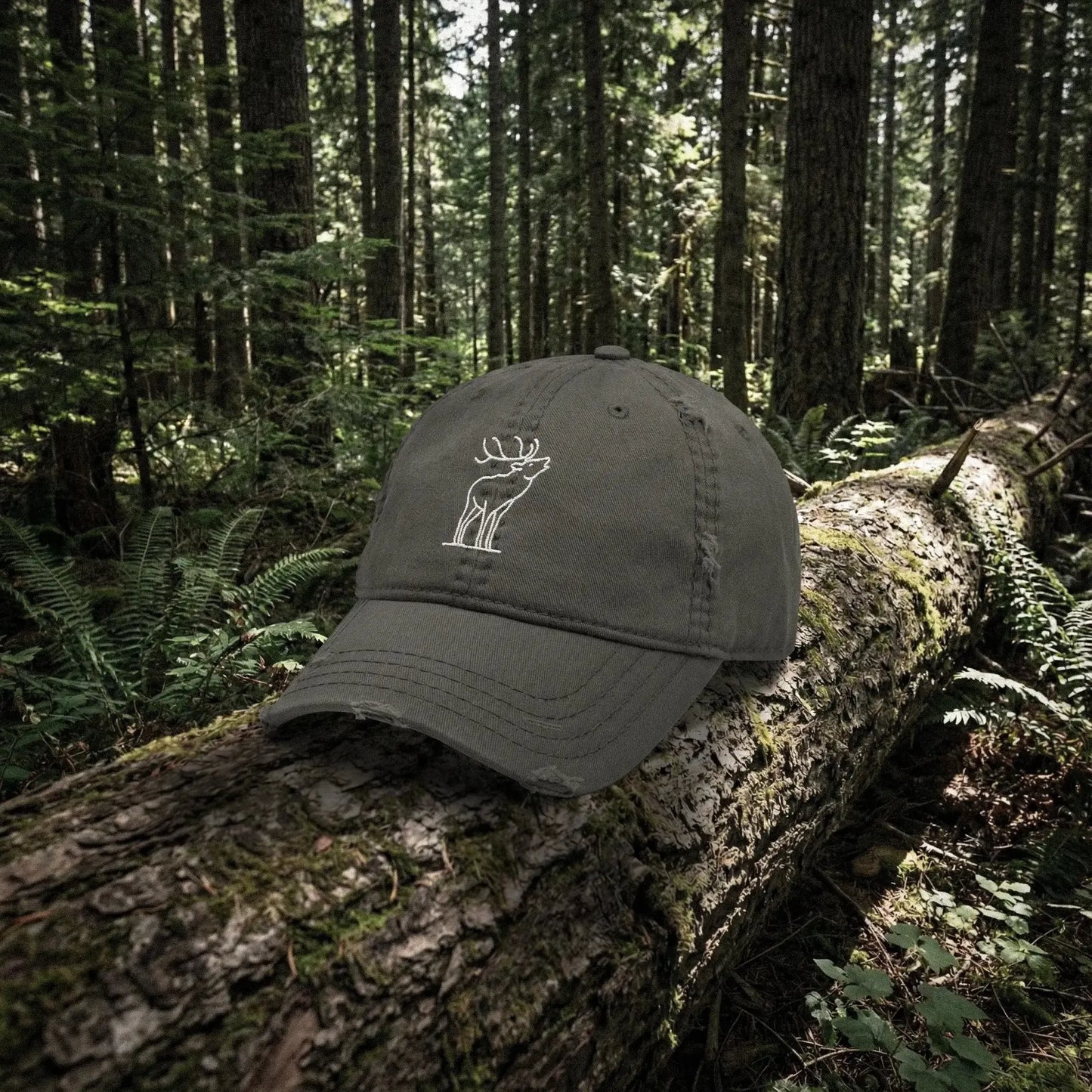 Dark gray cap with a white bugling elk embroidery on a log in a forest setting