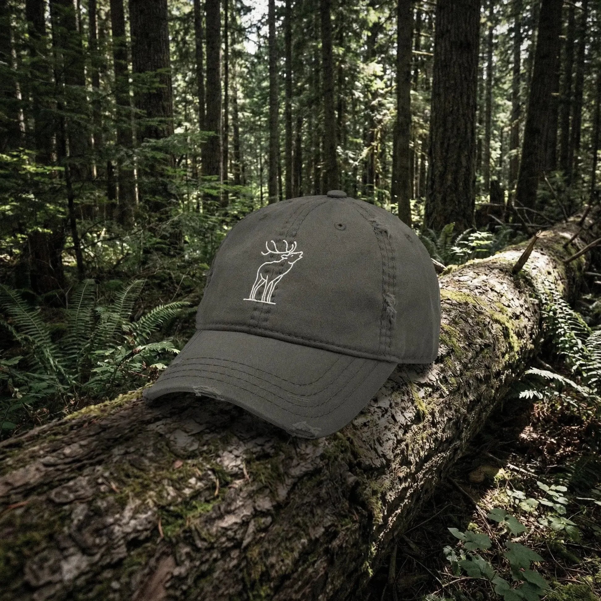 Dark gray cap with a white bugling elk embroidery on a log in a forest setting