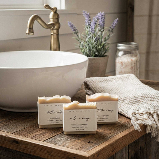 Three bars of soap on a wooden surface with a sink and lavender plant in the background.