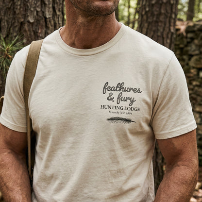 Man wearing a 'feathers & fury Hunting Lodge' t-shirt in a forest setting
