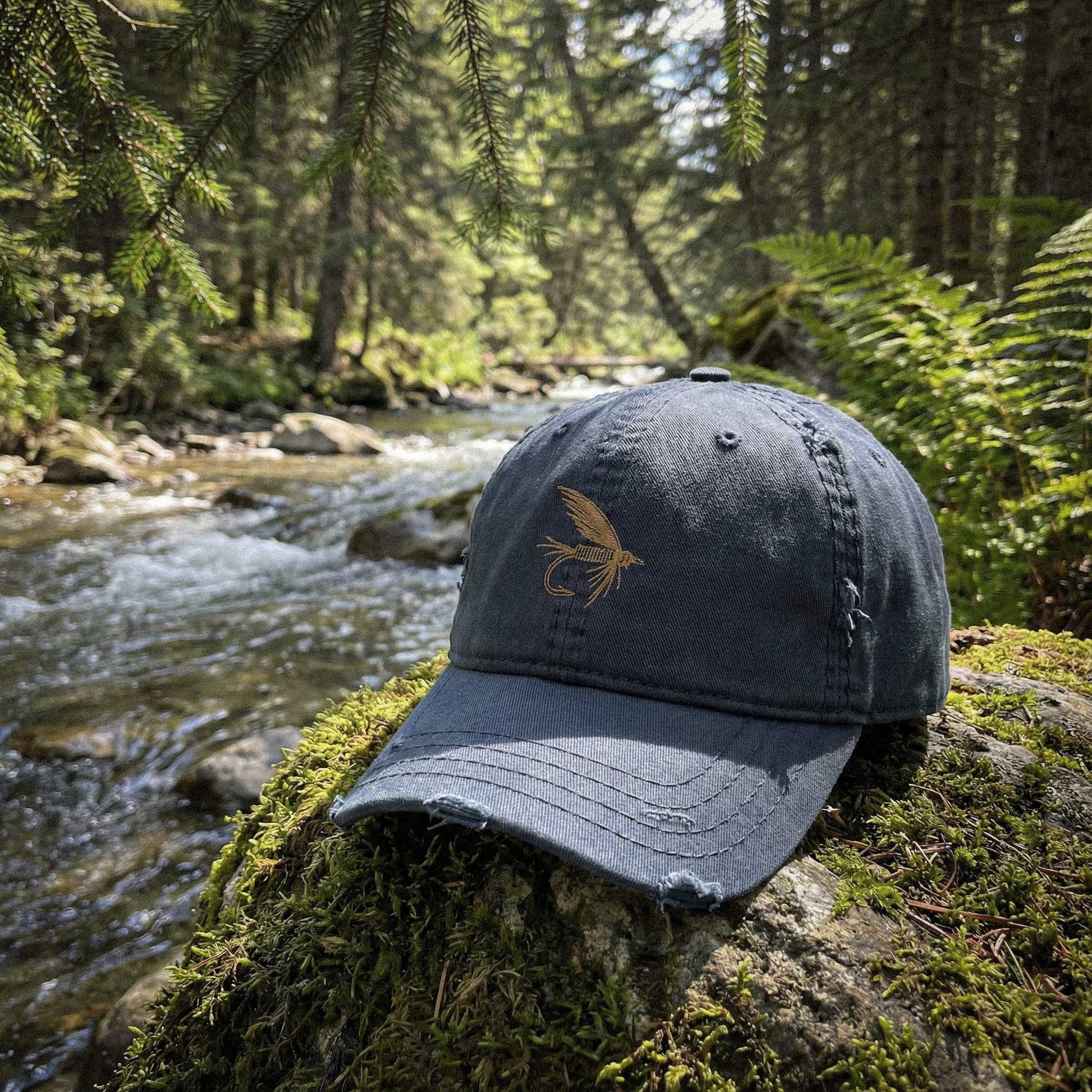 Blue cap with a fly design on a mossy rock by a forest stream