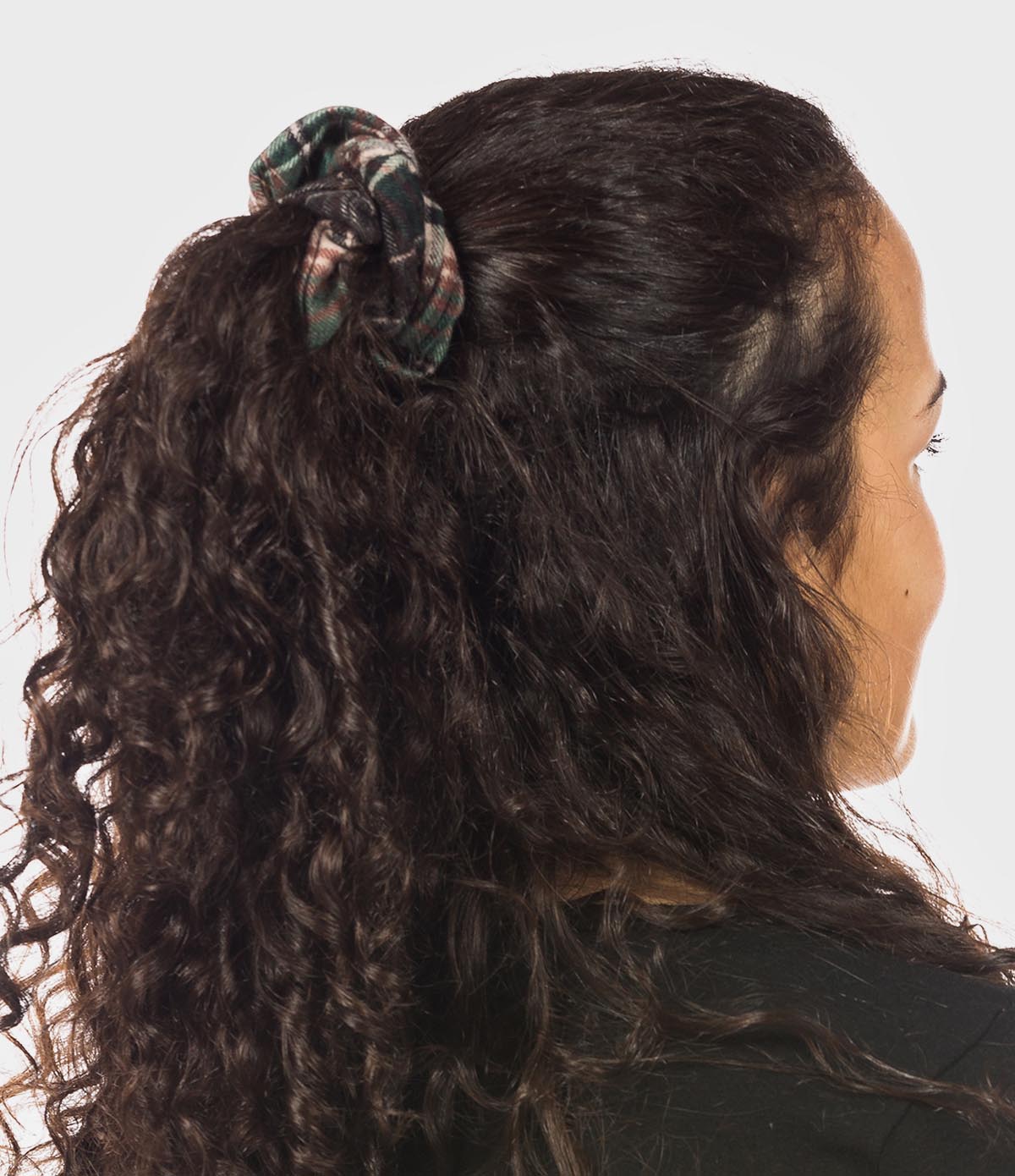Person with curly hair tied back with a brown flannel scrunchie on a white background.