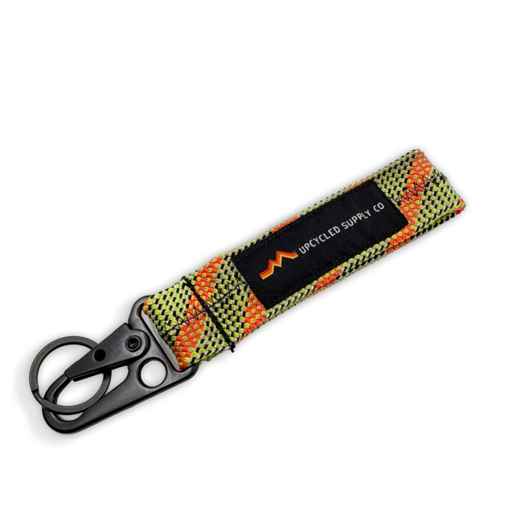 A green and orange braided climbing rope recycled fabric keychain with a black metal carabiner and a black label reading 'UPCYLED SUPPLY CO' on a white background.