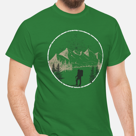 A green Unisex Cotton Tee on model, featuring a captivating hand-drawn illustration that encapsulates the spirit of hiking. Featuring majestic mountains and a compass rising in the sky that beckons the call of adventure. 