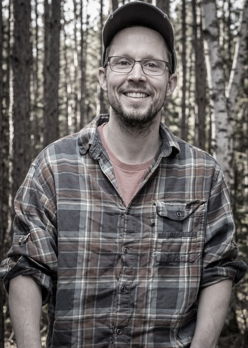 Artist and owner of Kempain Family Outfitters Jordan Kempain standing in the forest.