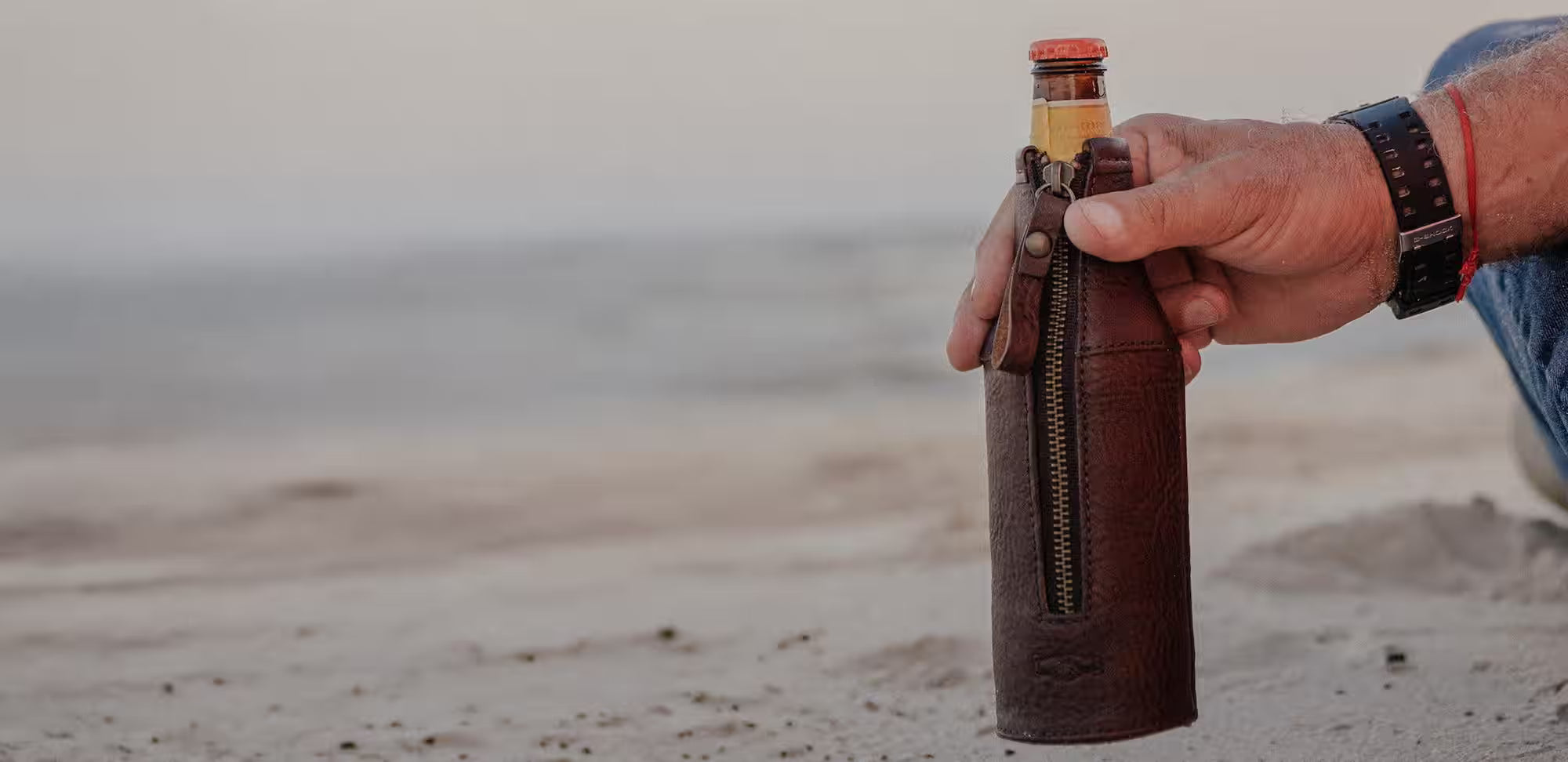 A leather beer Koozie photographed at the beach. 