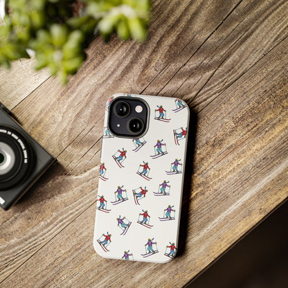 Lifestyle image of a cell phone case with illustrated skiers, lying flat on a desk, showcasing its vibrant mountain-inspired skiing pattern.